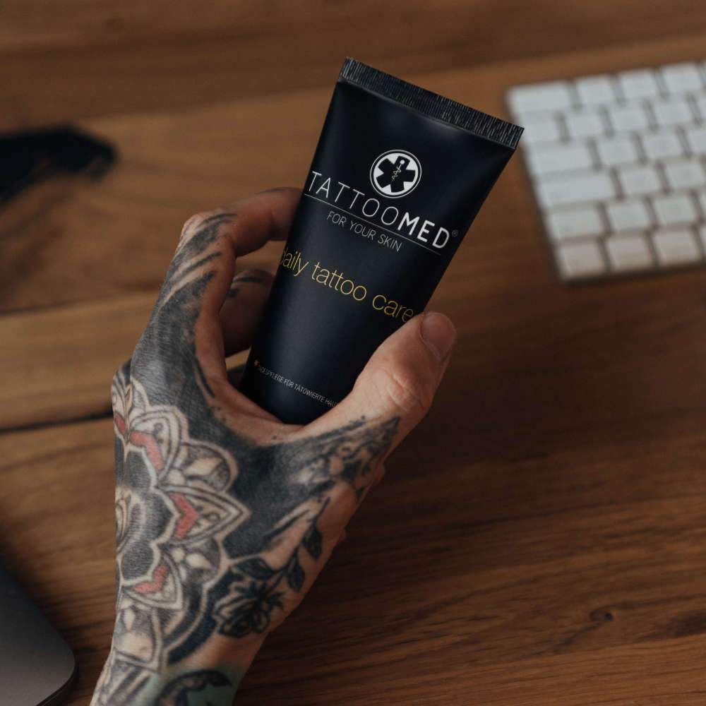 Getatoeëerde hand houdt TattooMed Daily Tattoo Care crème vast – dagelijkse verzorging en bescherming van tattoos