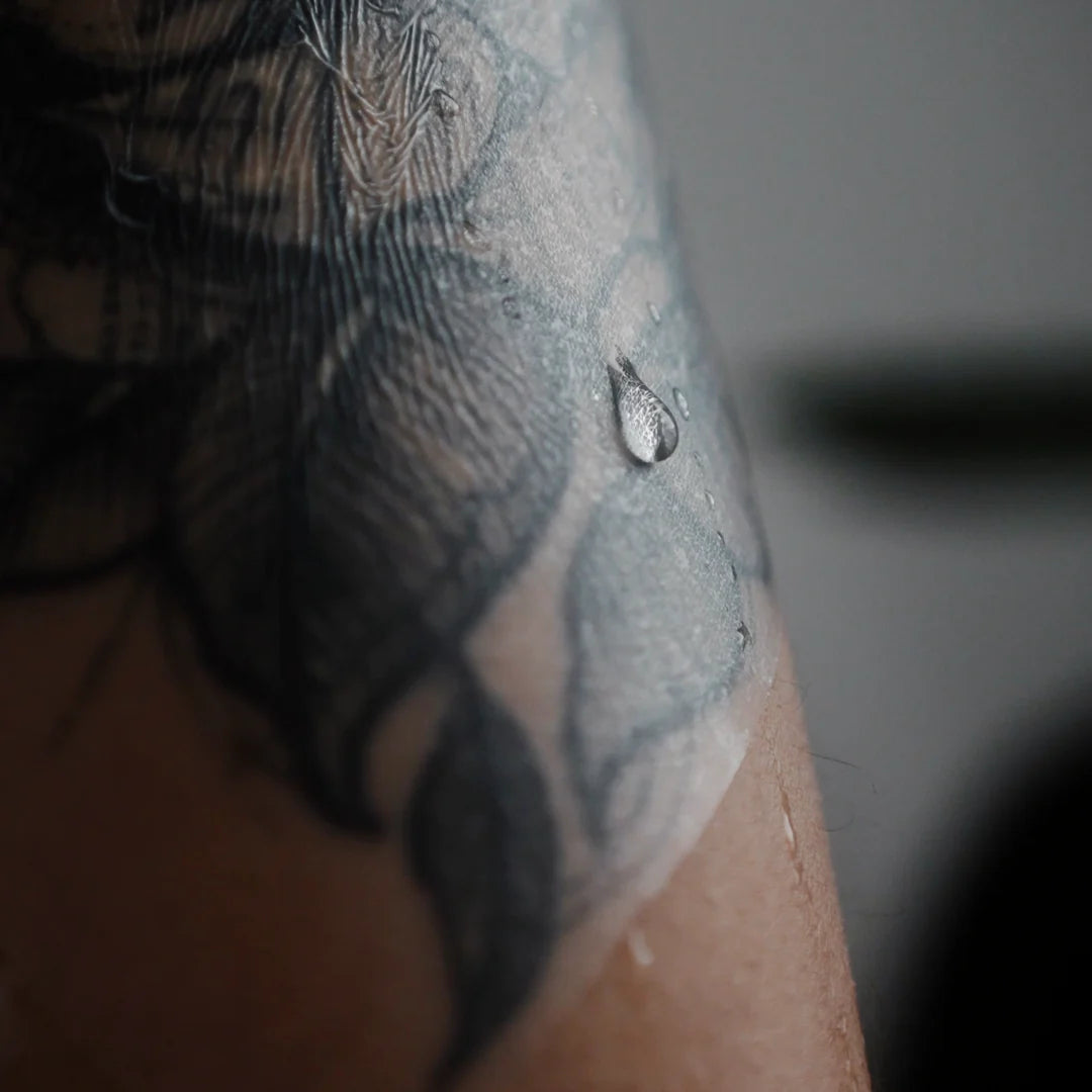 Close-up van tattoo onder TattooMed Protection Film met waterdruppel – ademende second skin folie voor tattoo nazorg